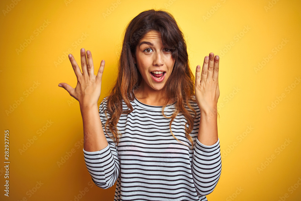 Young beautiful woman wearing stripes t-shirt standing over yelllow isolated background showing and pointing up with fingers number nine while smiling confident and happy. Young beautiful woman wearing stripes t-shirt standing over yelllow isolated background showing and pointing up with fingers number nine while smiling confident and happy.