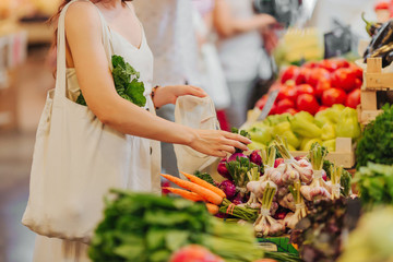Female hands puts fruits and vegetables in cotton produce bag at food market. Reusable eco bag for shopping. Zero waste concept.