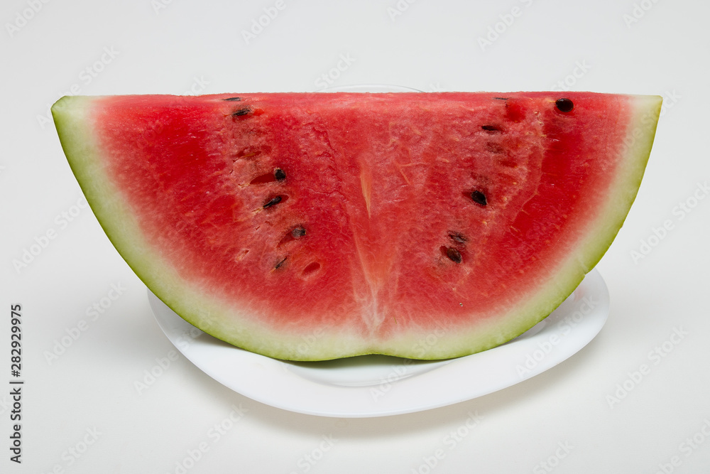 slice of watermelon on a white plate white background red green seeds black
