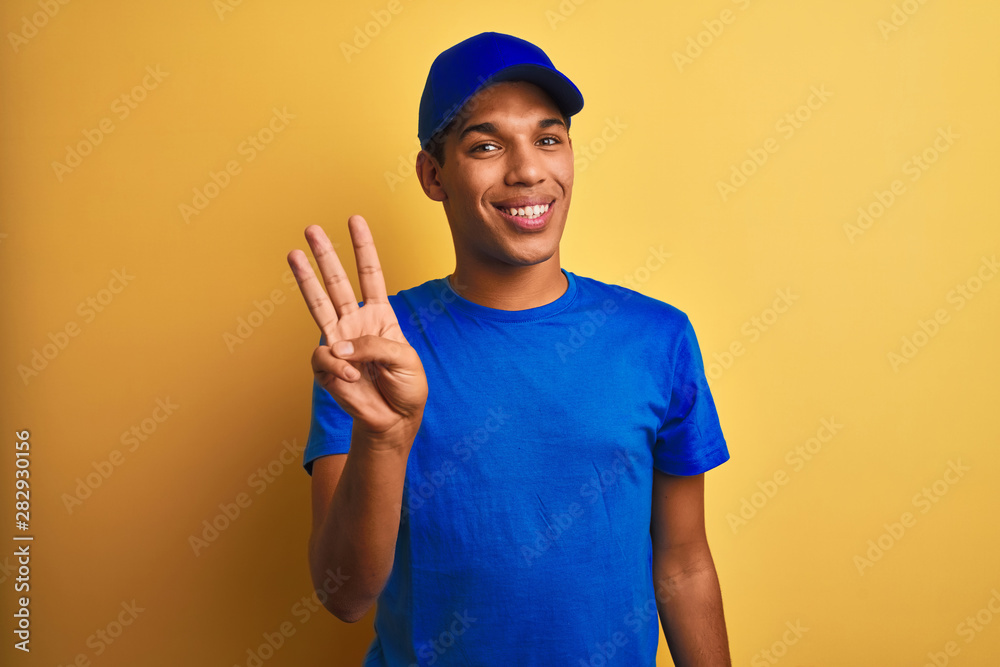 Young handsome arab delivery man standing over isolated yellow background showing and pointing up with fingers number three while smiling confident and happy.