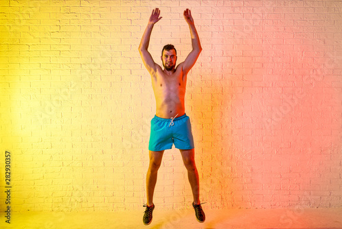 Young sporty man performs a jump on a yellow background.