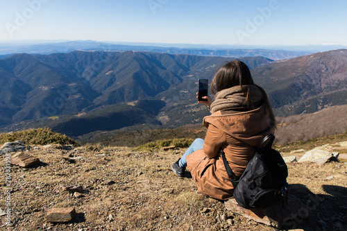 Beautiful woman sitting after hiking and taking photo with phone during winter or autumn in Catalonia