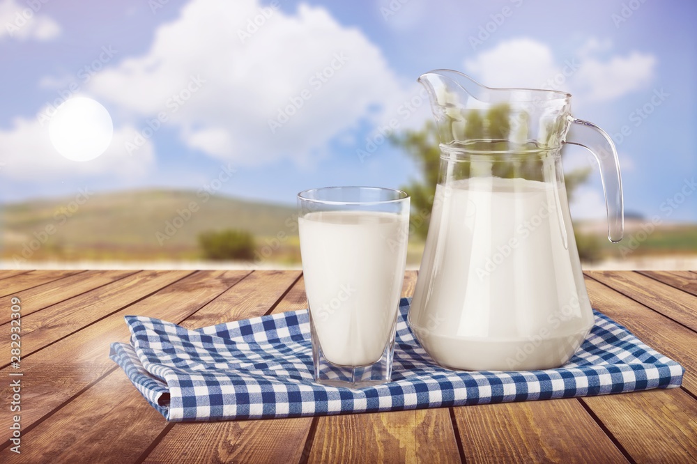 Glass of milk and jar on table with cloth and background