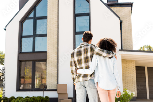 back view of african american couple hugging while looking at new house