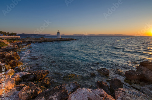 Wild coast of the Aegina island and the old small lighthouse in the background, Saronic gulf, Greece, at sunset. © Aron M  - Austria