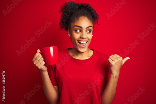 Young african american woman drinking a cup of coffee over isolated red background pointing and showing with thumb up to the side with happy face smiling