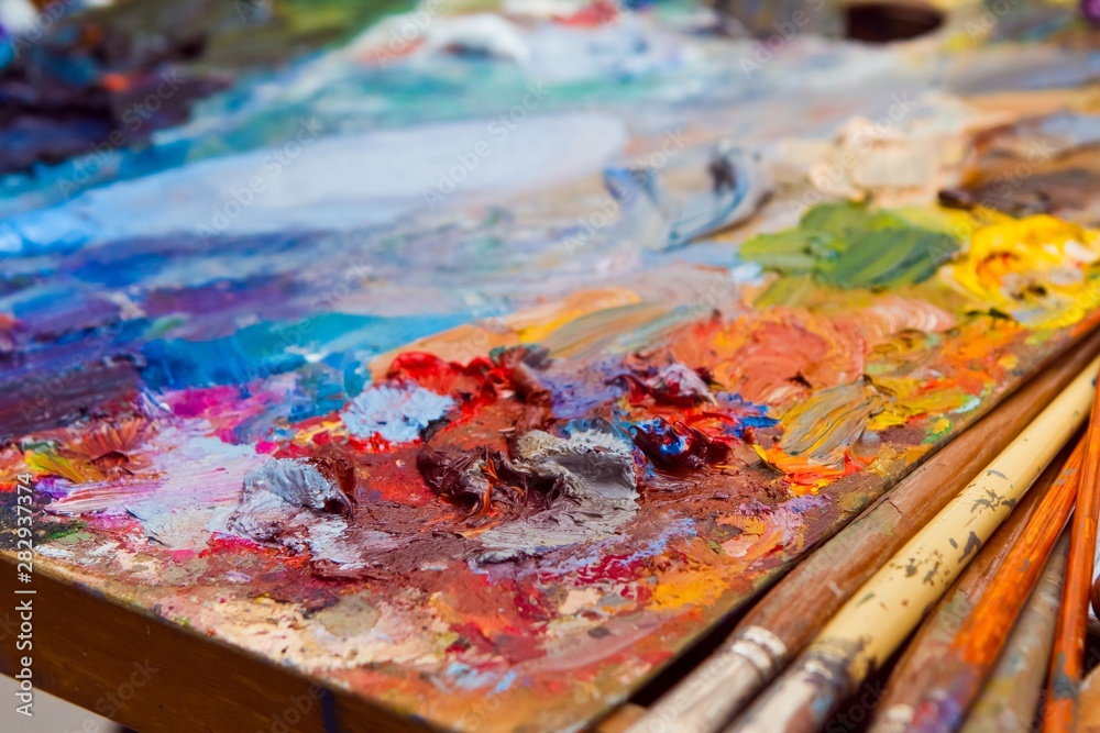 painter's wooden palette in disorder with mixed fresh bright oil paints at summer plainair painting session painter's wooden palette in disorder with mixed fresh bright oil paints at summer plainair painting session