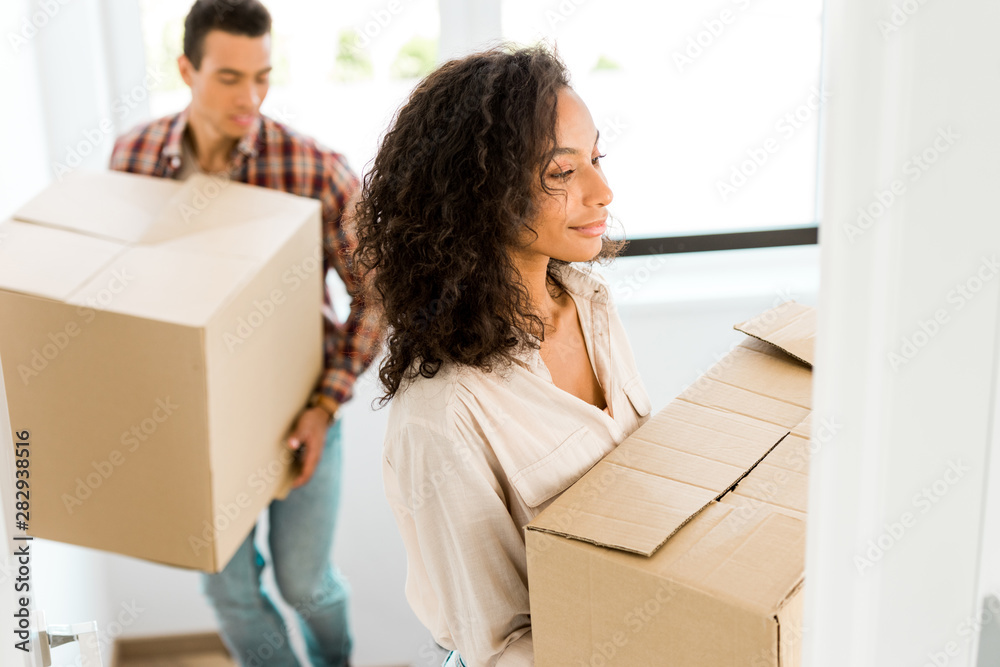 selective focus of african american woman holding box while man going upstairs selective focus of african american woman holding box while man going upstairs