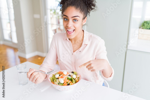 Young african american woman eating healthy pasta salad very happy pointing with hand and finger