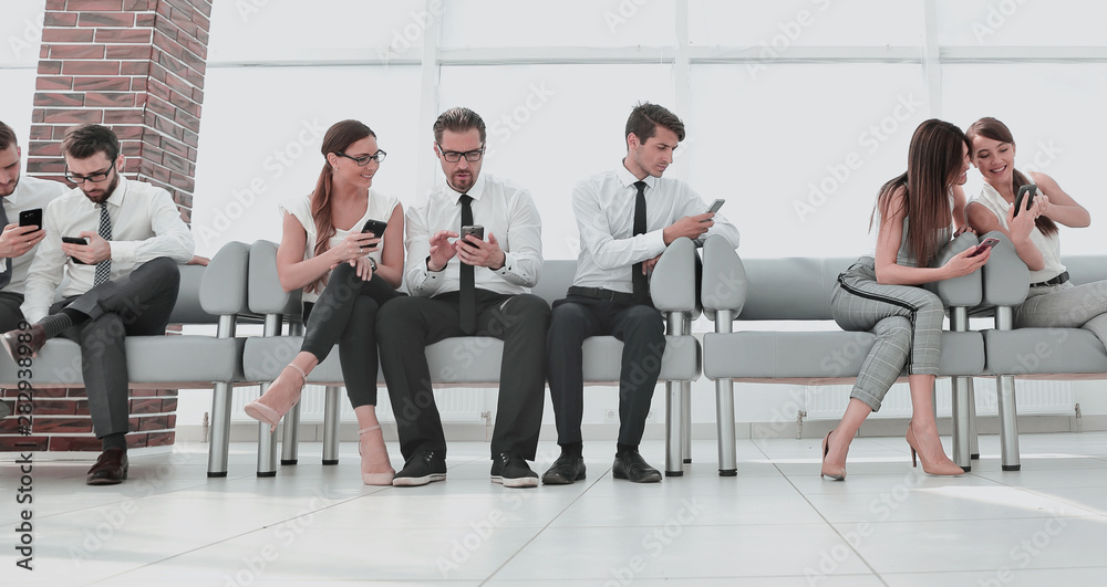 business colleagues using their smartphones sitting in the lobby of the office business colleagues using their smartphones sitting in the lobby of the office