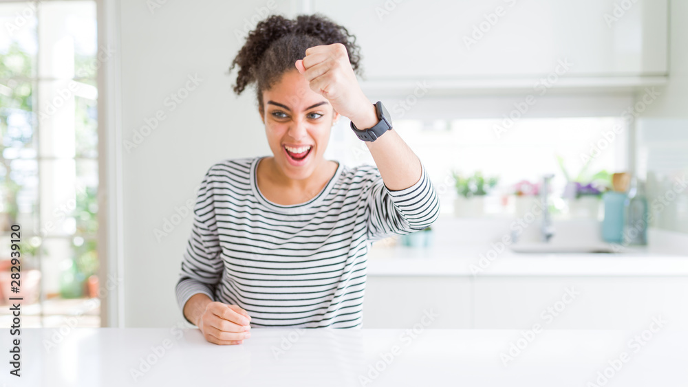 Beautiful african american woman with afro hair wearing casual striped sweater angry and mad raising fist frustrated and furious while shouting with anger. Rage and aggressive concept. Beautiful african american woman with afro hair wearing casual striped sweater angry and mad raising fist frustrated and furious while shouting with anger. Rage and aggressive concept.