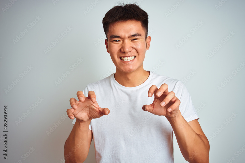 Young asian chinese man wearing t-shirt standing over isolated white background smiling funny doing claw gesture as cat, aggressive and sexy expression Young asian chinese man wearing t-shirt standing over isolated white background smiling funny doing claw gesture as cat, aggressive and sexy expression
