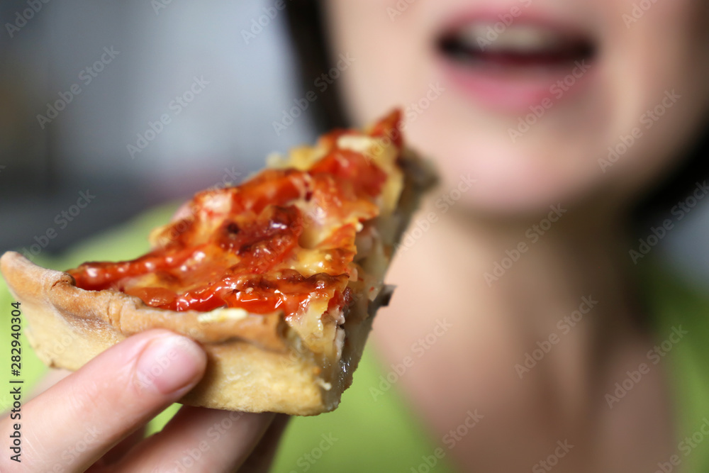 Girl eating and enjoying pizza. Appetizing piece of pie with cheese, meat and tomatoes in female hand close-up