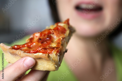 Girl eating and enjoying pizza. Appetizing piece of pie with cheese, meat and tomatoes in female hand close-up