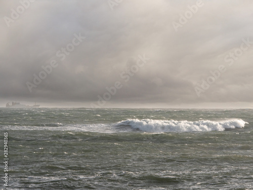 Ocean's waves, Dramatic cloudy sky, Ship silhouette on the horizon.