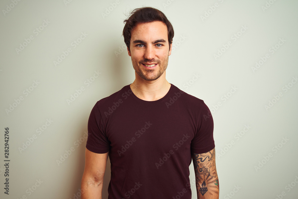 Young handsome man with tattoo wearing purple casual t-shirt over isolated white background with a happy and cool smile on face. Lucky person.