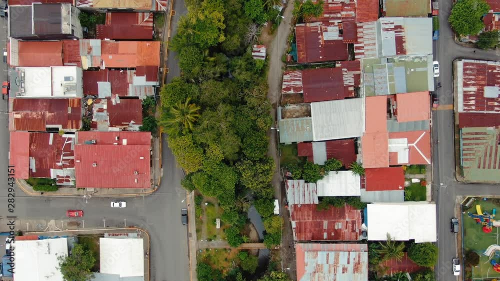 Drone Footage of Downtown Quepos, Costa Rica with Normal Traffic Driving Through The Streets, Big Green Trees, and Rusty Metal Laminate Rooftops, Camera Hovering Dolly-In