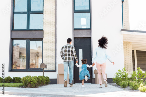 back view of african american couple with child running to new house