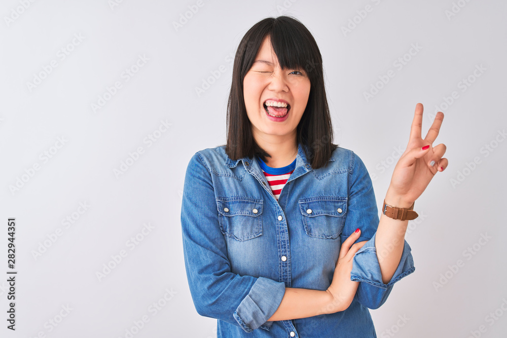 Young beautiful chinese woman wearing denim shirt over isolated white background smiling with happy face winking at the camera doing victory sign. Number two. Young beautiful chinese woman wearing denim shirt over isolated white background smiling with happy face winking at the camera doing victory sign. Number two.