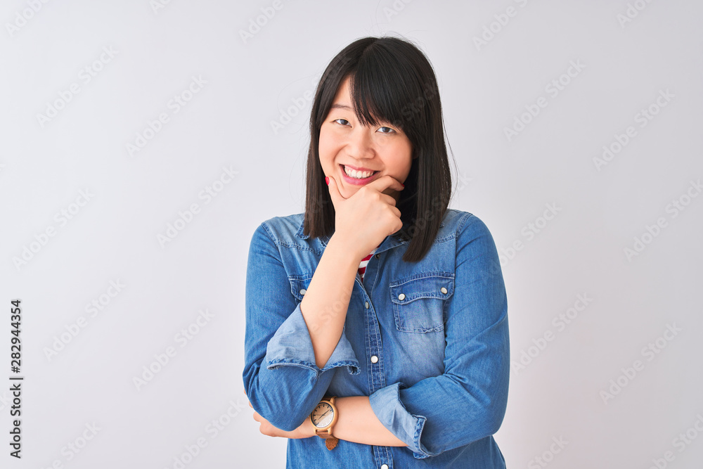 Young beautiful chinese woman wearing denim shirt over isolated white background looking confident at the camera smiling with crossed arms and hand raised on chin. Thinking positive. Young beautiful chinese woman wearing denim shirt over isolated white background looking confident at the camera smiling with crossed arms and hand raised on chin. Thinking positive.