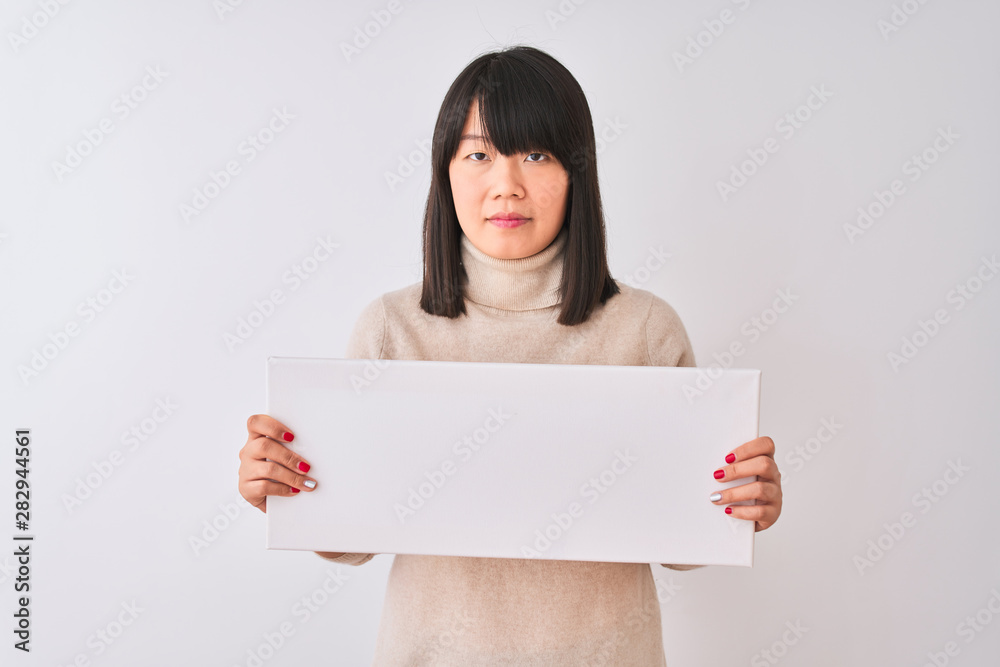 Young beautiful Chinese woman holding banner standing over isolated white background with a confident expression on smart face thinking serious Young beautiful Chinese woman holding banner standing over isolated white background with a confident expression on smart face thinking serious