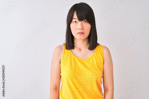 Young beautiful chinese woman wearing yellow t-shirt over isolated white background with serious expression on face. Simple and natural looking at the camera.