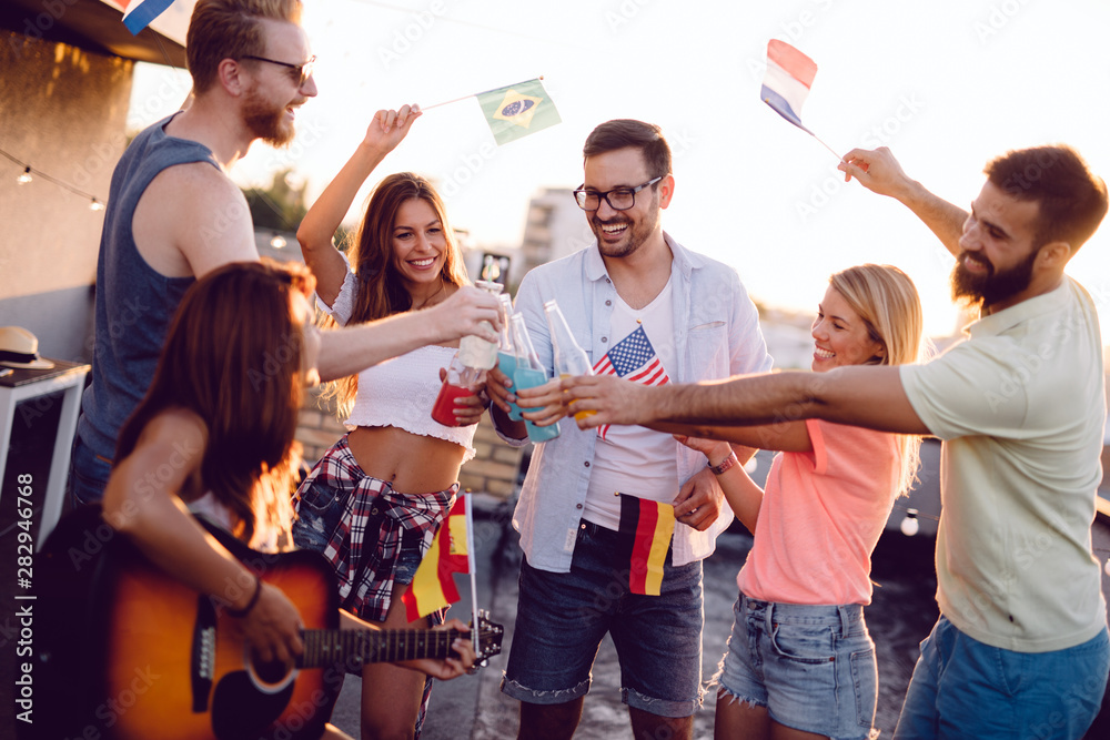 Obraz premium Young friends having fun at a rooftop party, playing the guitar, singing, dancing and drinking