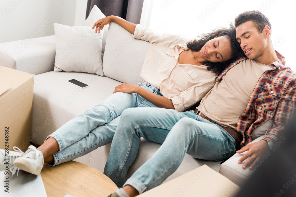 full length view of african american wife and husband sleeping while sitting on sofa full length view of african american wife and husband sleeping while sitting on sofa