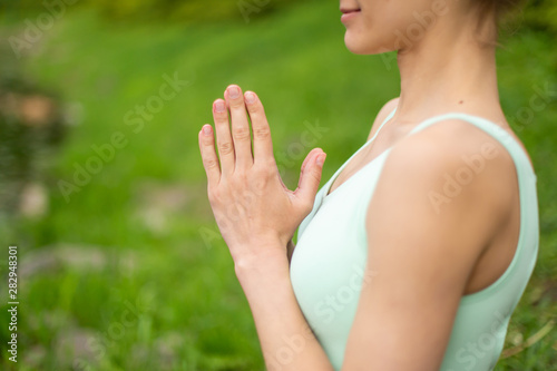 Thin brunette girl plays sports and performs beautiful and sophisticated yoga poses in a summer park. Green forest and the river on the background. Woman doing exercises on the yoga mat. Lotus pose