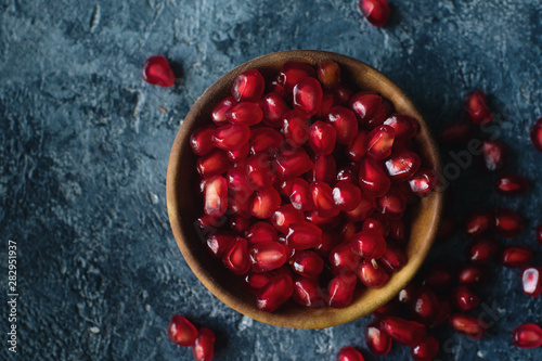 Fresh organic juicy pomegranate seeds in wooden bowl on dark stone background