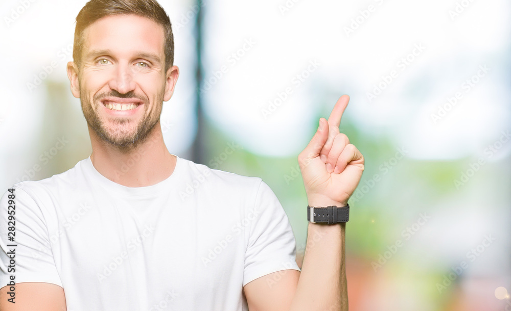 Handsome man wearing casual white t-shirt with a big smile on face, pointing with hand and finger to the side looking at the camera. Handsome man wearing casual white t-shirt with a big smile on face, pointing with hand and finger to the side looking at the camera.