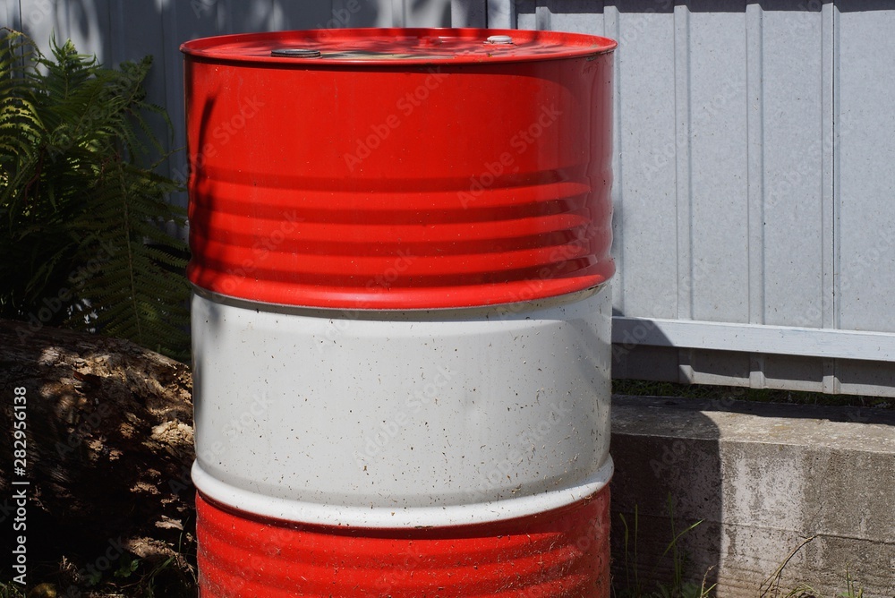 a large metal red white barrel stands outside against a gray wall a large metal red white barrel stands outside against a gray wall