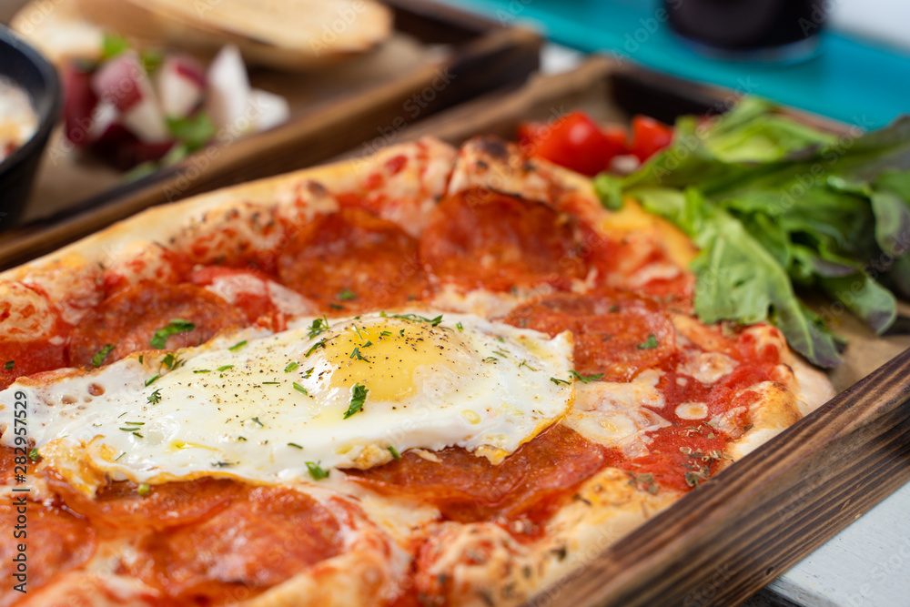 Close up of mouthwatering rome pizza with crust, tomato sauce, spicy pepperoni and fried egg in the centre Close up of mouthwatering rome pizza with crust, tomato sauce, spicy pepperoni and fried egg in the centre