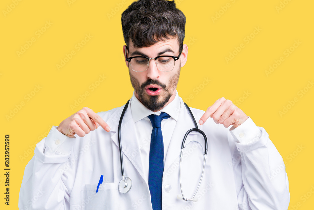 Young doctor man wearing hospital coat over isolated background Pointing down with fingers showing advertisement, surprised face and open mouth Young doctor man wearing hospital coat over isolated background Pointing down with fingers showing advertisement, surprised face and open mouth