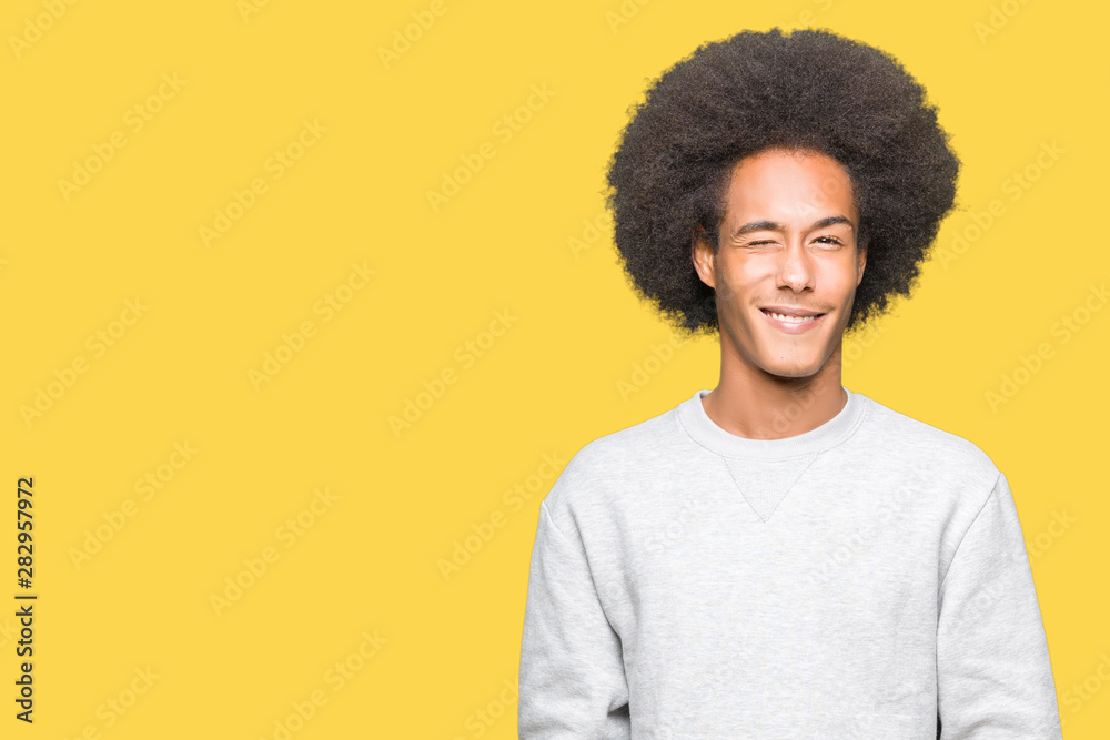 Young african american man with afro hair wearing sporty sweatshirt winking looking at the camera with sexy expression, cheerful and happy face. Young african american man with afro hair wearing sporty sweatshirt winking looking at the camera with sexy expression, cheerful and happy face.