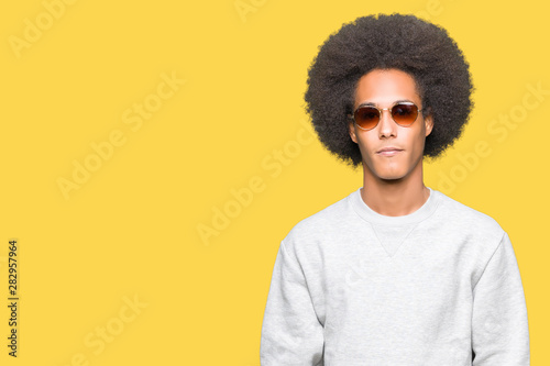 Young african american man with afro hair wearing sunglasses with serious expression on face. Simple and natural looking at the camera. © Krakenimages.com