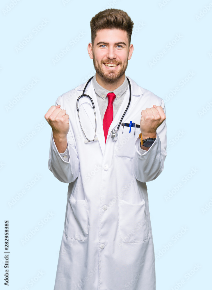 Young handsome doctor man wearing medical coat celebrating surprised and amazed for success with arms raised and open eyes. Winner concept. Young handsome doctor man wearing medical coat celebrating surprised and amazed for success with arms raised and open eyes. Winner concept.