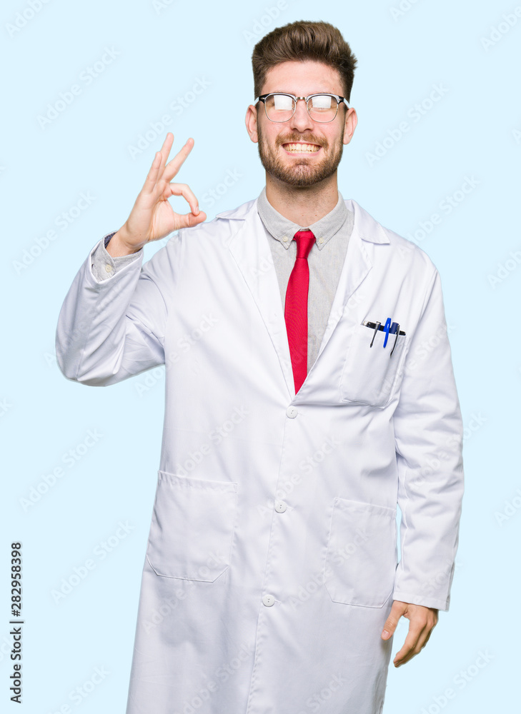 Young handsome scientist man wearing glasses smiling positive doing ok sign with hand and fingers. Successful expression. Young handsome scientist man wearing glasses smiling positive doing ok sign with hand and fingers. Successful expression.