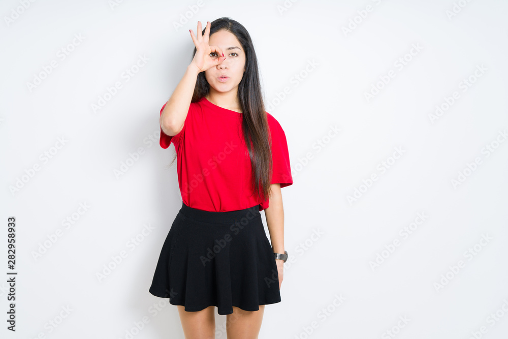 Beautiful brunette woman wearing red t-shirt and skirt over isolated background doing ok gesture shocked with surprised face, eye looking through fingers. Unbelieving expression. Beautiful brunette woman wearing red t-shirt and skirt over isolated background doing ok gesture shocked with surprised face, eye looking through fingers. Unbelieving expression.