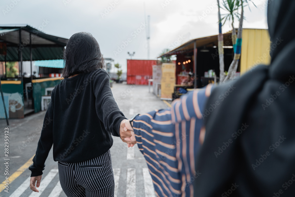 back view of two friends walking together with holding hands back view of two friends walking together with holding hands