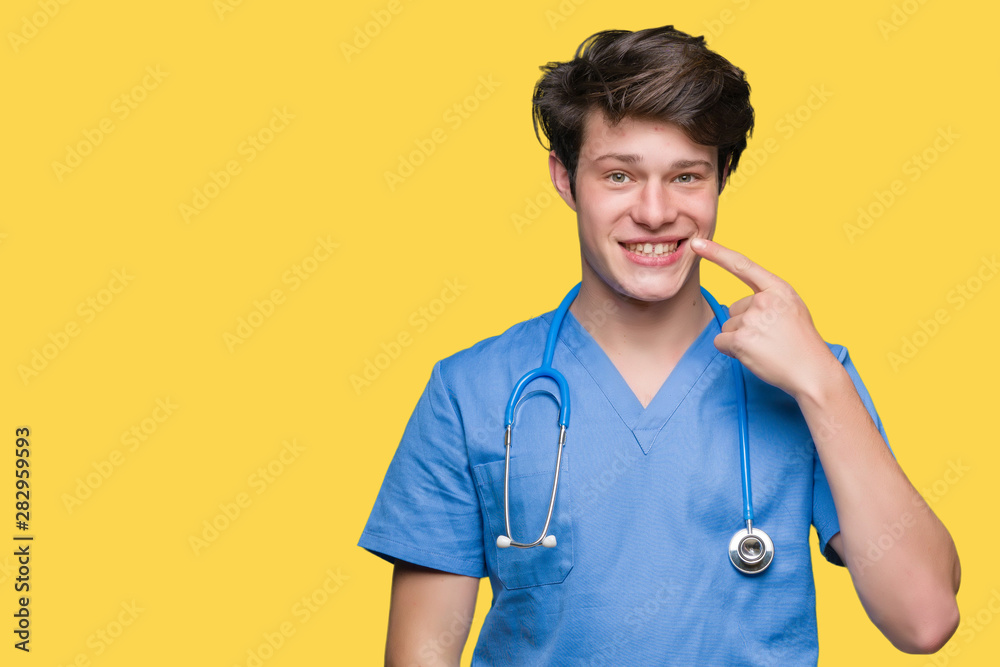 Young doctor wearing medical uniform over isolated background Pointing with hand finger to face and nose, smiling cheerful