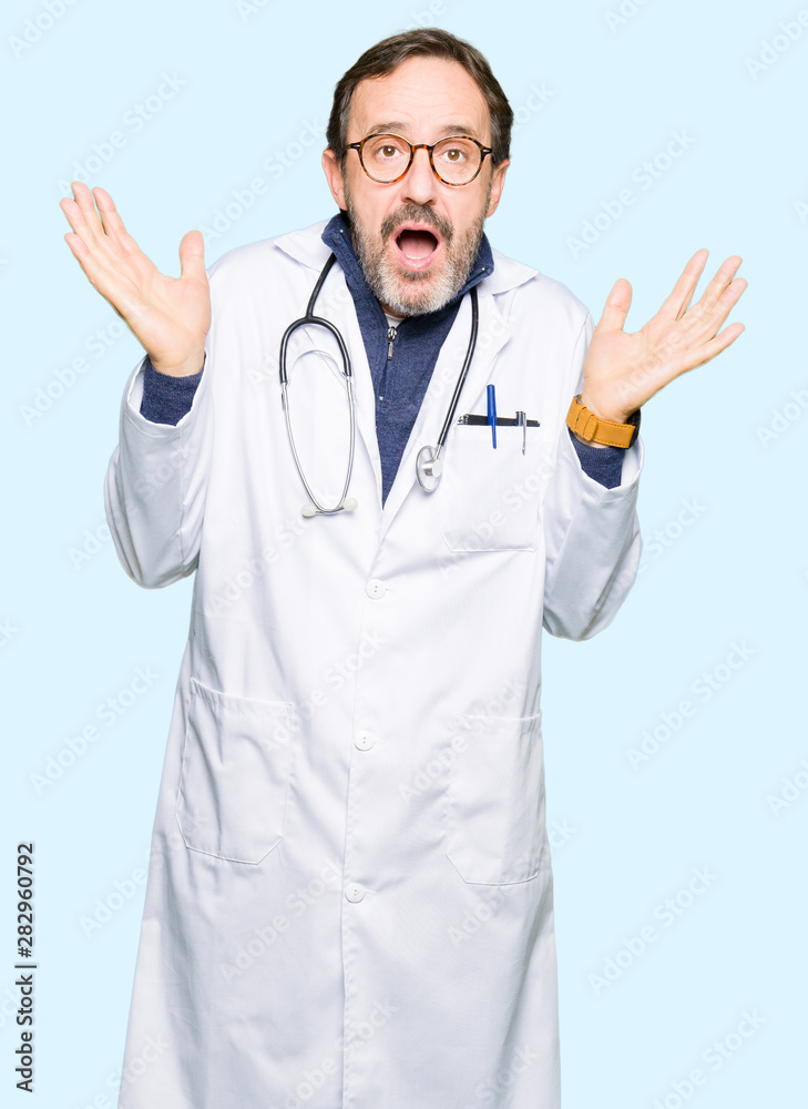 Handsome middle age doctor man wearing medical coat clueless and confused expression with arms and hands raised. Doubt concept. Handsome middle age doctor man wearing medical coat clueless and confused expression with arms and hands raised. Doubt concept.