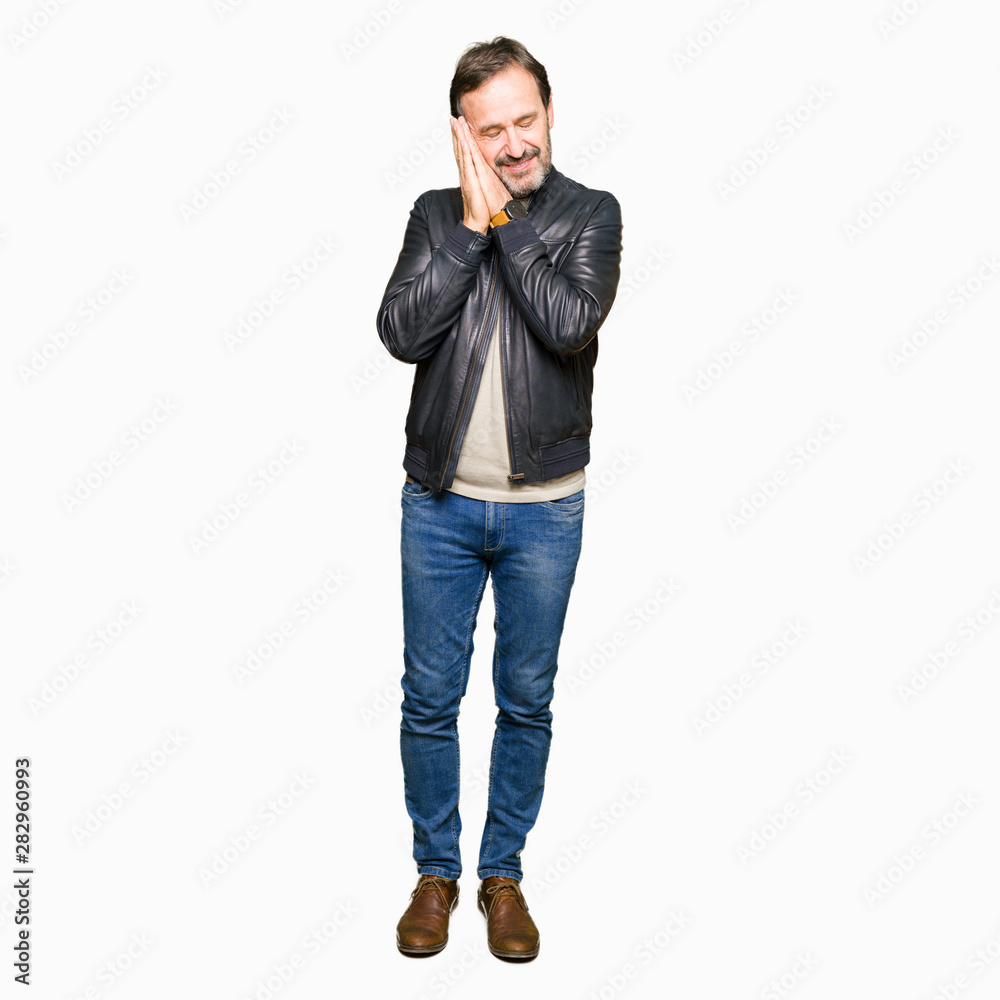 Middle age handsome man wearing black leather jacket sleeping tired dreaming and posing with hands together while smiling with closed eyes.