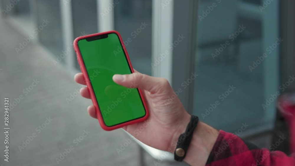 Close up hands man holding a smartphone touching phone with vertical green screen red case on background walk near airport street message business male device digital equipment internet slow motion
