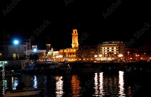 Tower of the provincial administration building seen at night with lights reflections in the Adriatic sea from the medieval castle Castello Svevo. Bari, Apulia, Southern Italy
