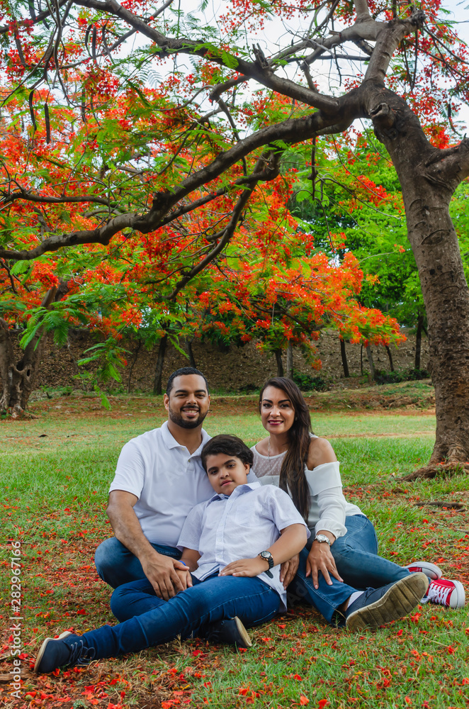 couple of Latin American men and women, with boy suffers autism, happy in a portrait family outdoors together in a park, the three laughing hugging