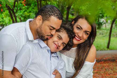 couple of Latin American men and women, with boy suffers autism, happy in a portrait family outdoors together in a park, the three laughing hugging © Francisco