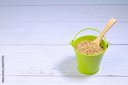 Green bucket full of quinoa with a wooden spoon inside on white background.