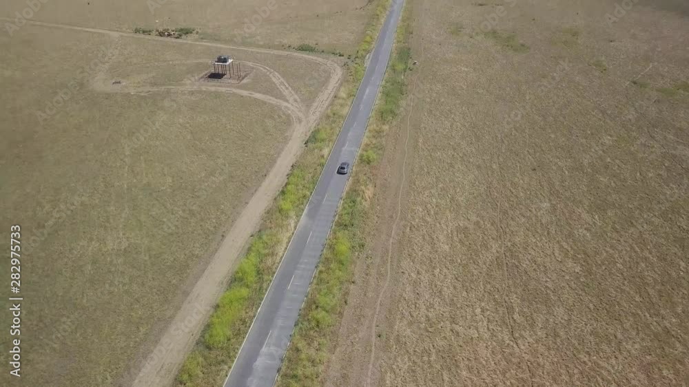 4K Aerial shot of silver SUV driving down long straight country road, isolated against wide open golden desolate fields as camera pulls back and reveals wide expanse and horizon with hills and sky 4K Aerial shot of silver SUV driving down long straight country road, isolated against wide open golden desolate fields as camera pulls back and reveals wide expanse and horizon with hills and sky
