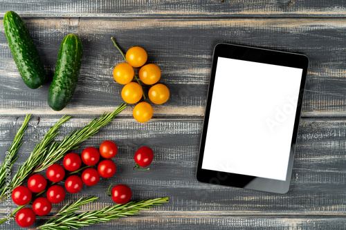 red and yellow cherry tomatoes  rosemary  cucumbers and tablet pc on black wooden table. Mock up vegetarian menu  vegetable salad recipe.